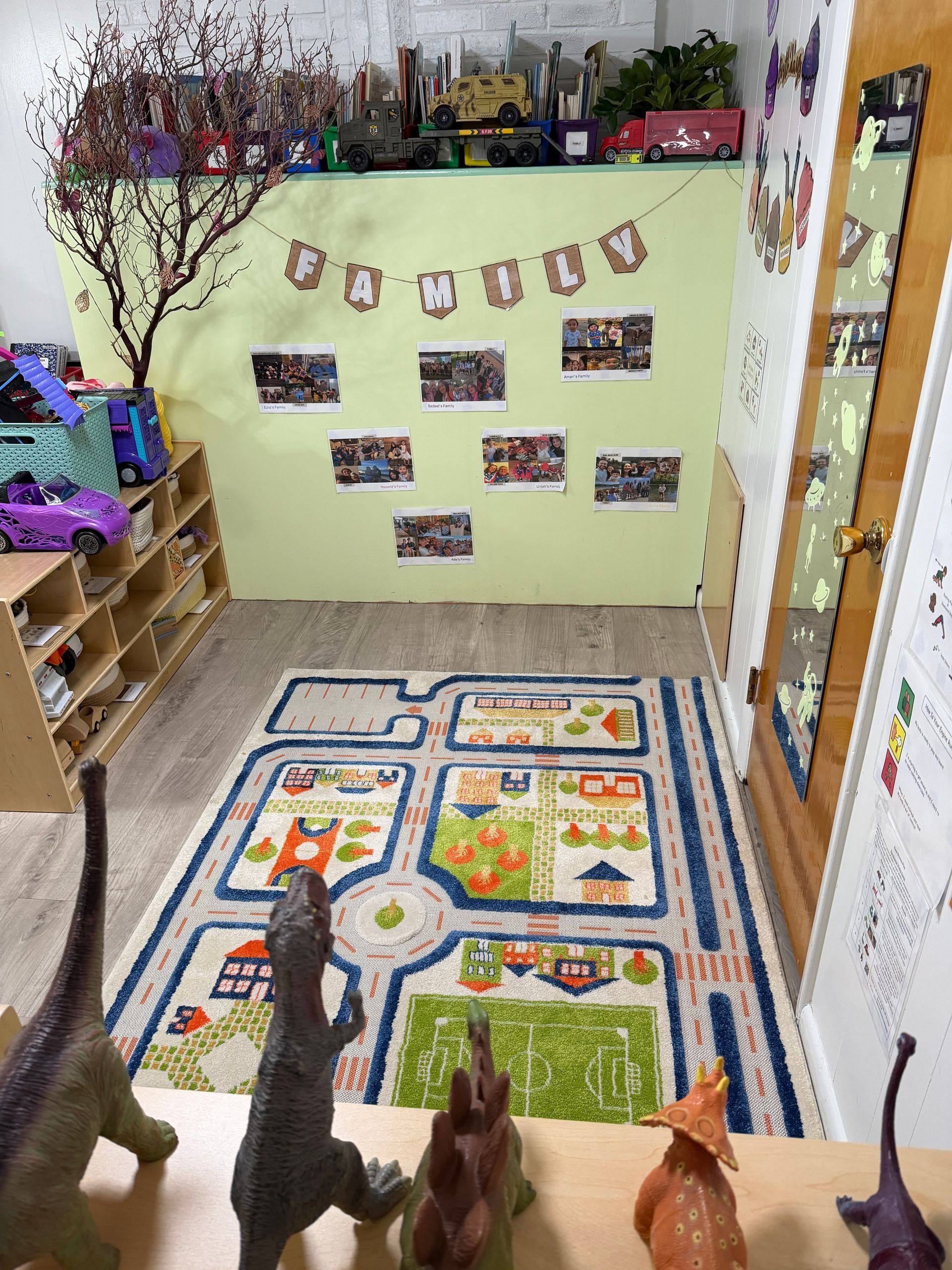 Colorful classroom corner with a wall display, rugs on the floor, and toy animals lined up in the foreground