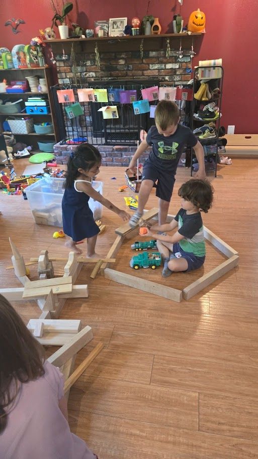 Children playing with blocks on a wooden floor in a colorful classroom with shelves of toys and supplies.
