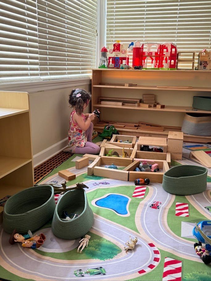 Child playing on the floor with toys and a road mat in a bright room with shelves and blinds