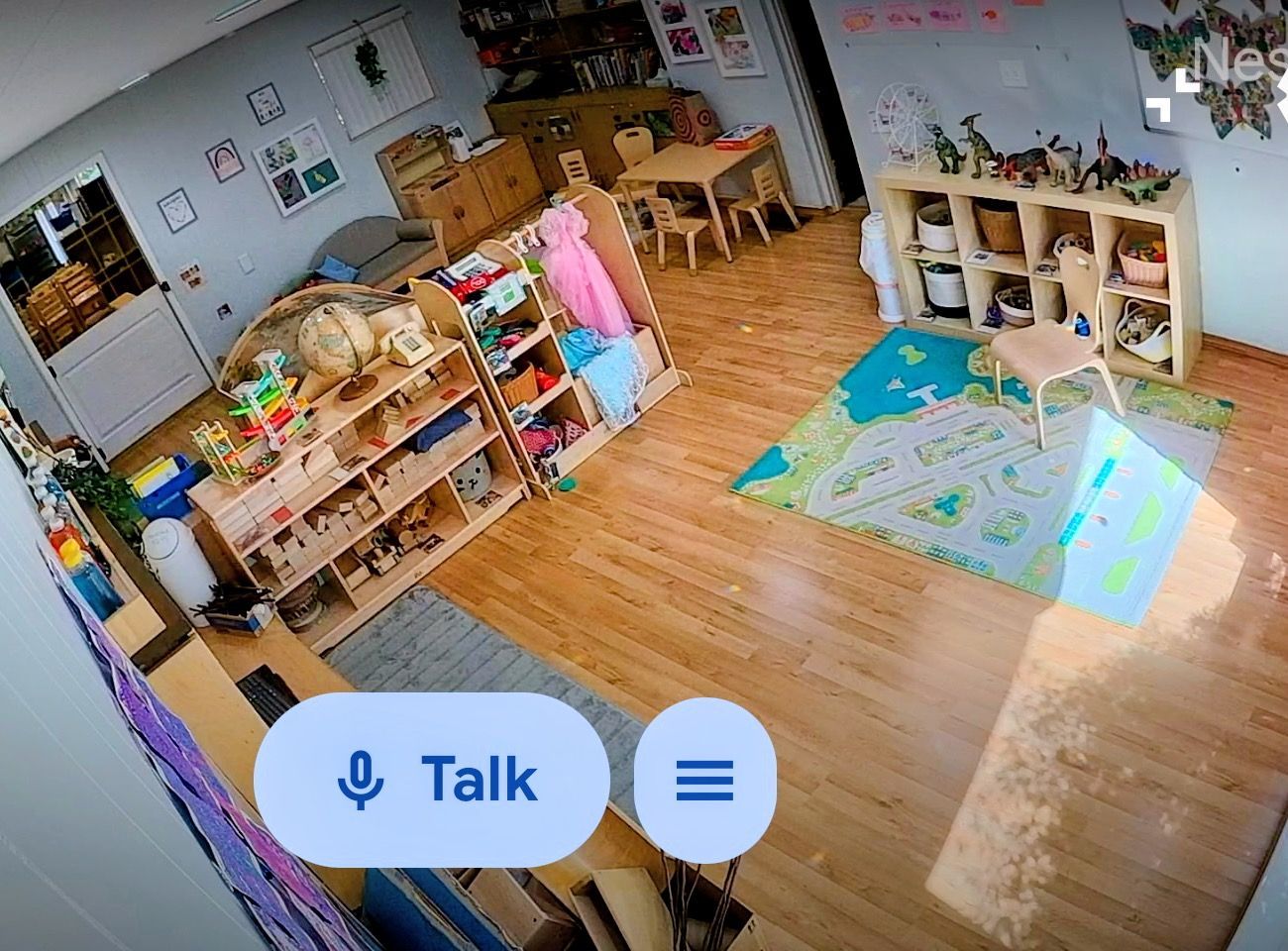 Wide-angle view of a tidy daycare classroom with shelves, tables, toys, and a colorful play mat on the floor