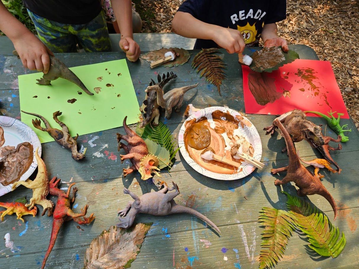 Children examining toy dinosaurs on colorful paper at a craft table