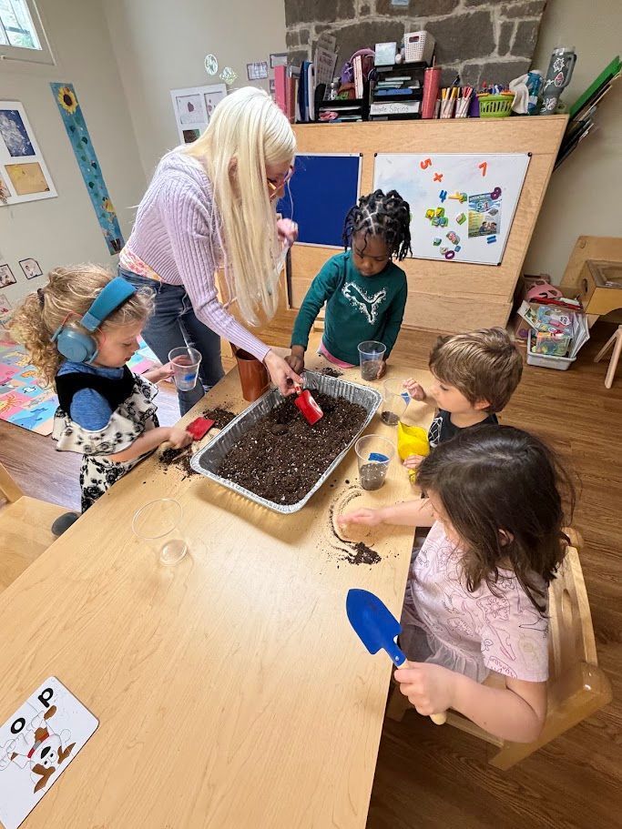 Teacher helping children plant seeds in a tray at a classroom table