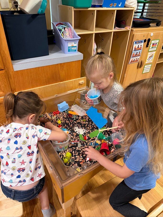 Children play with colorful sensory materials at a classroom table.