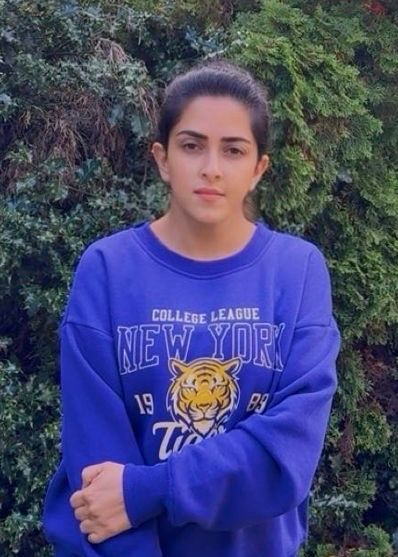 Person in a blue New York sweatshirt standing in front of green foliage.