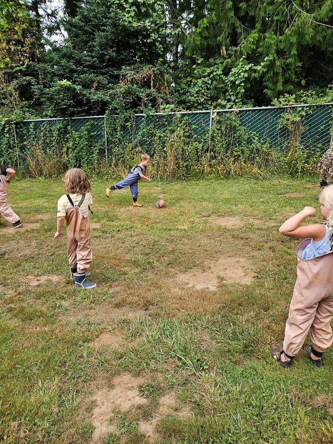 Children playing in a grassy yard near a chain-link fence and trees