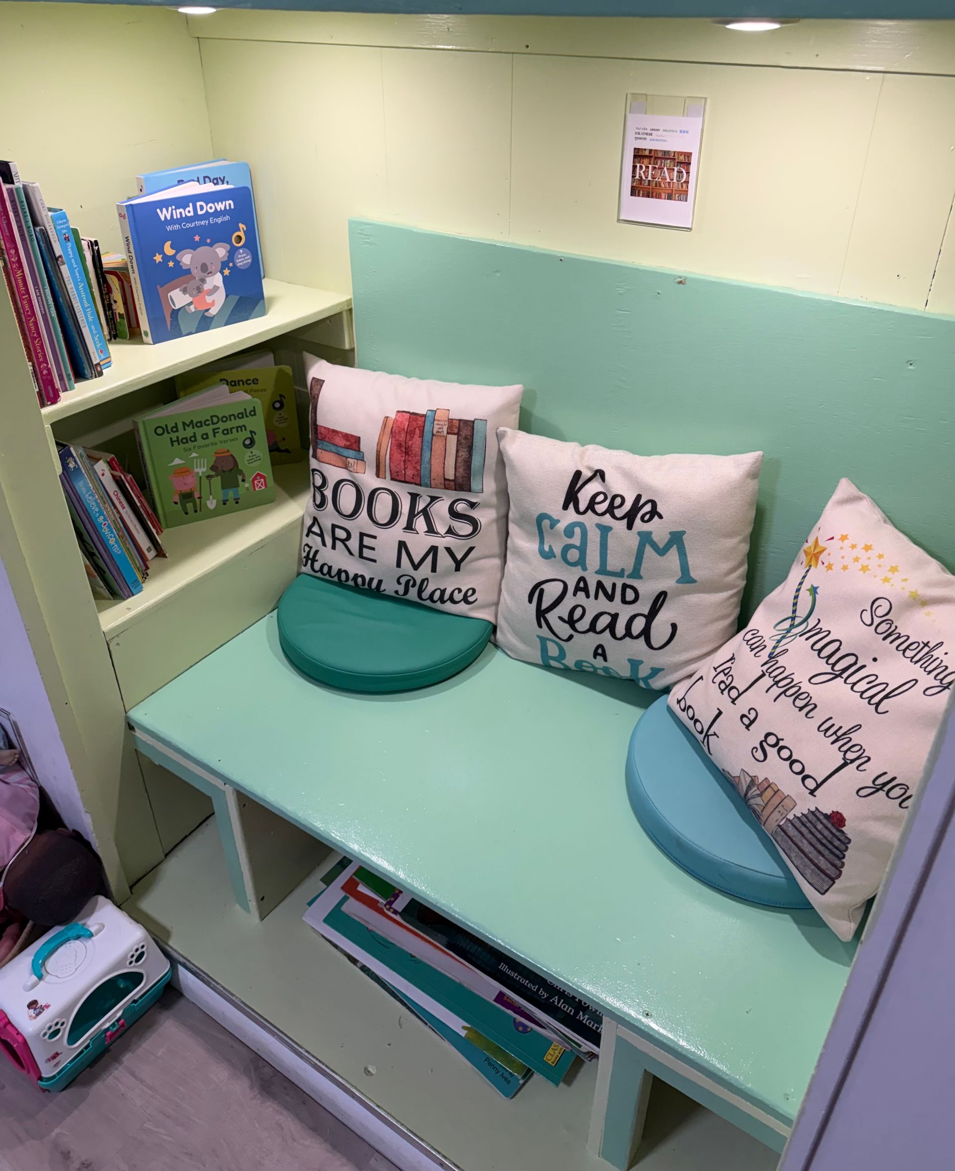 Cozy reading nook with mint bench, pillows, and bookshelves in a small library corner.