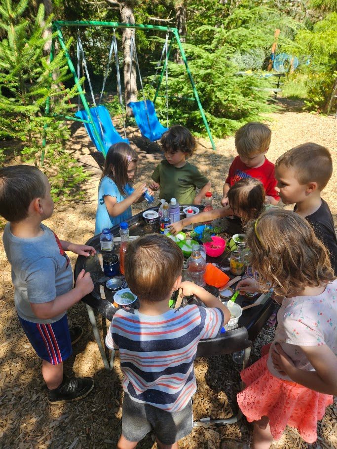 Children gathered around a table outdoors, sharing snacks and playing in a sunny garden