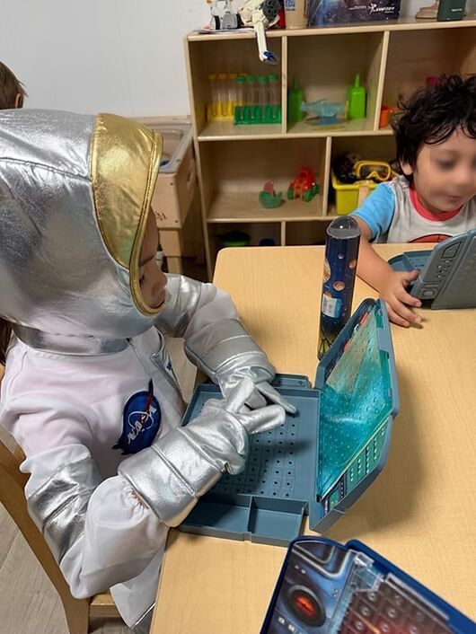 Child in silver astronaut costume playing a card game at a classroom table