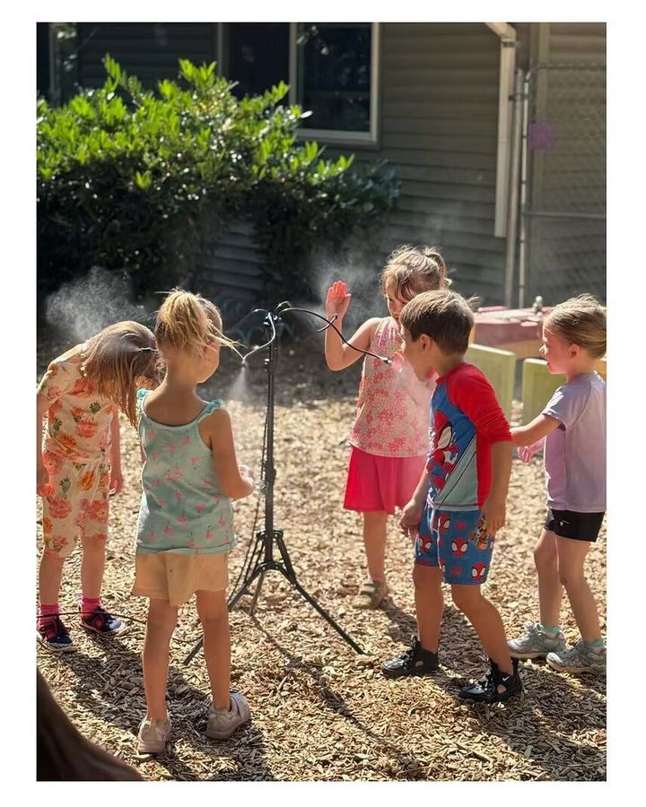 Five children play in a sprinkler outdoors on a sunny day.