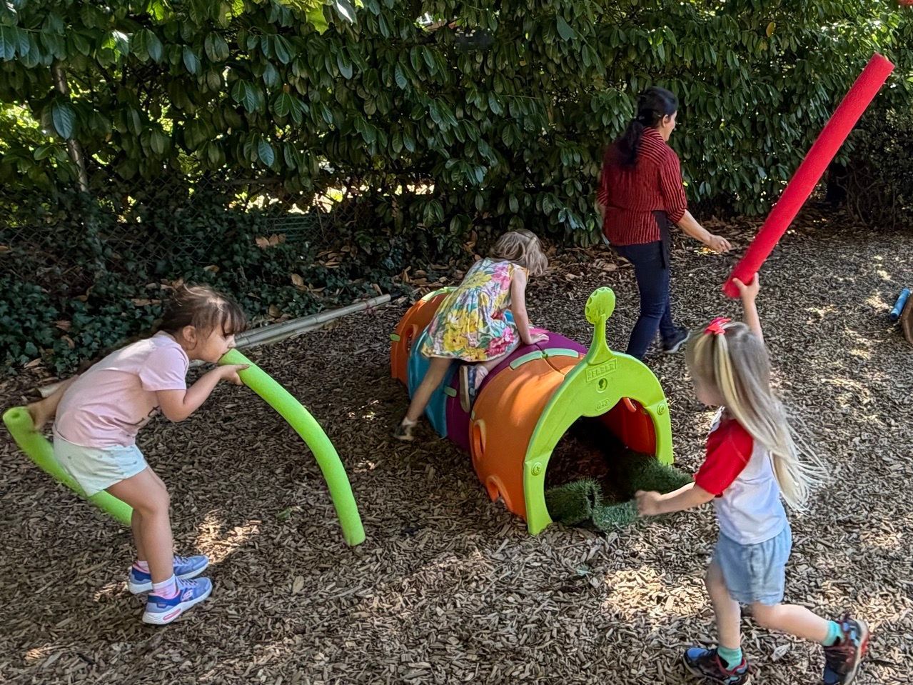 Children play with colorful tube tunnels in a woodchip playground.