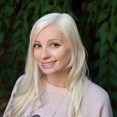 Blonde woman smiling in a light pink top against a leafy green background