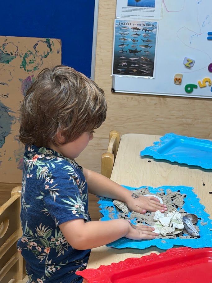 Child at a table playing with white sensory foam on a blue tray in a classroom.