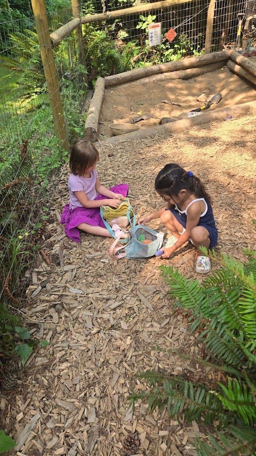 Two children playing in a dirt garden path with toys, surrounded by wooden borders and greenery.