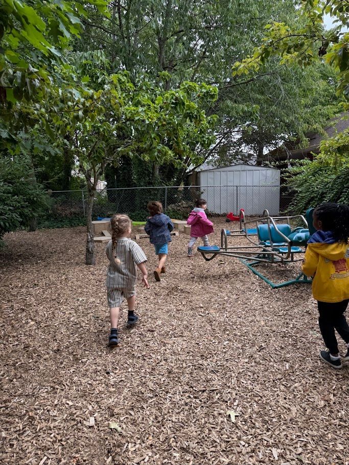 Children walking along a wooded playground path beside blue play equipment and a white shed