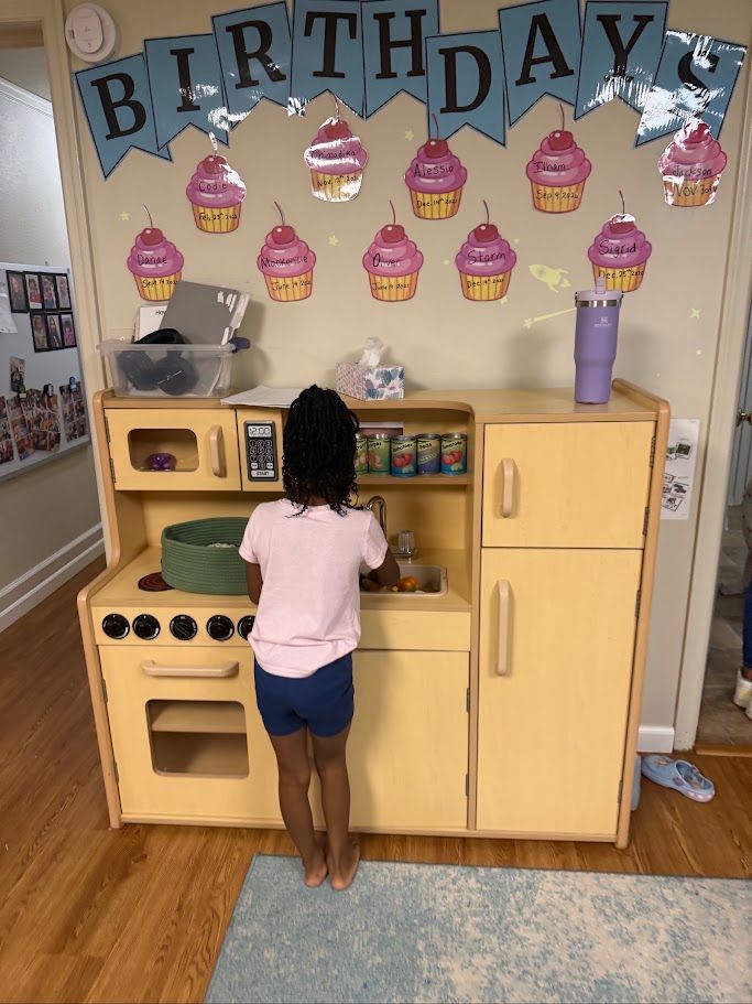 Child playing at a toy kitchen under a “BIRTHDAY” banner with cupcake decorations.