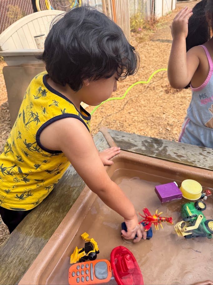 Child playing with toy cars and figures in a sandbox outdoors.