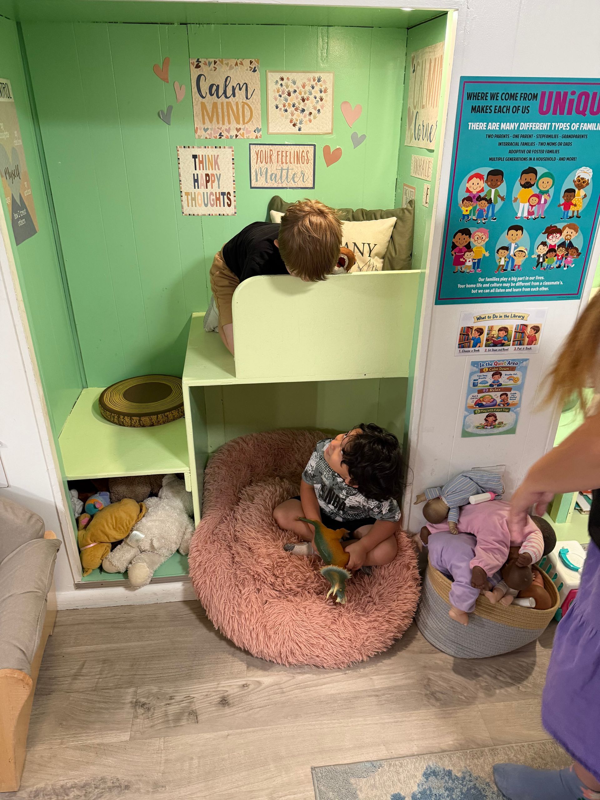 Children playing in a pastel-green play nook with stuffed animals, posters, and pillows.