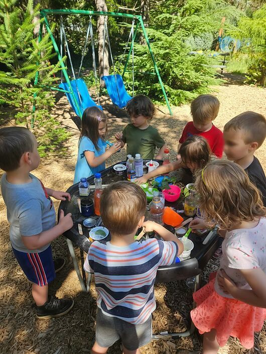Children gathered around a table outdoors, sharing food and drinks in a sunny garden.