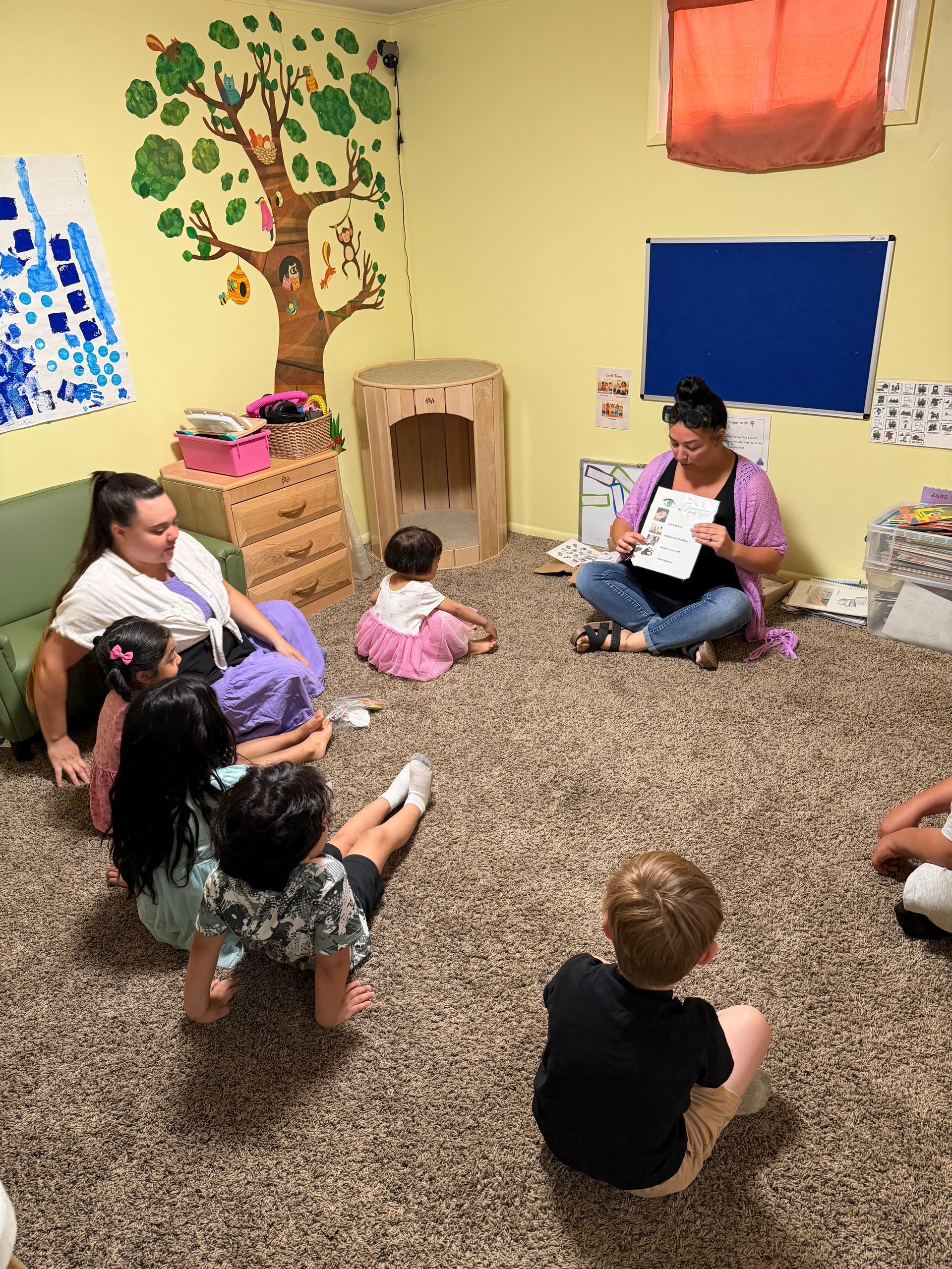 People sitting in a circle on the floor during a classroom story time with a teacher reading a book