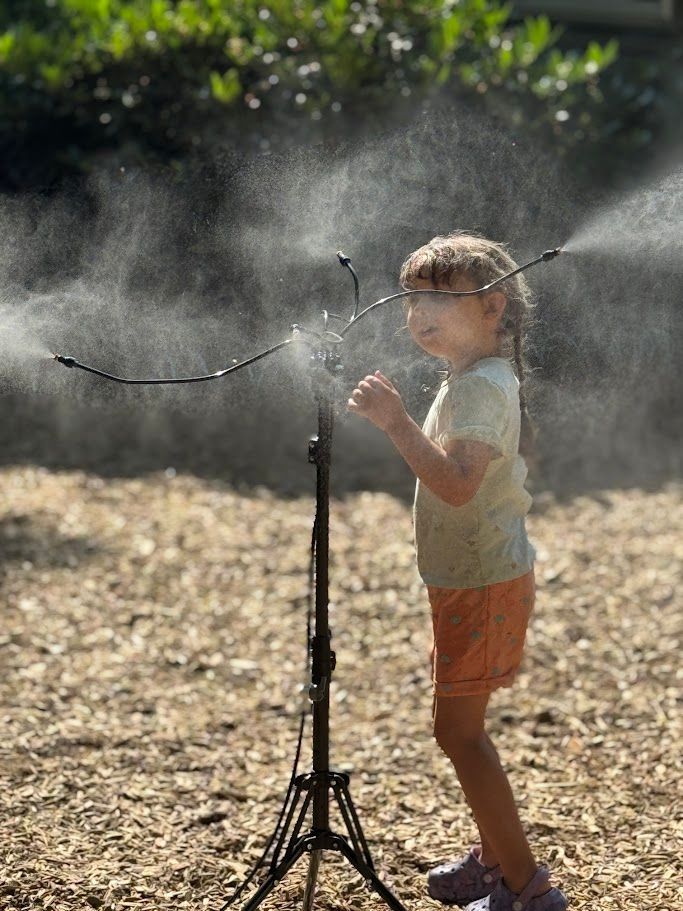 Child playing in a misting sprinkler outdoors on a sunny day