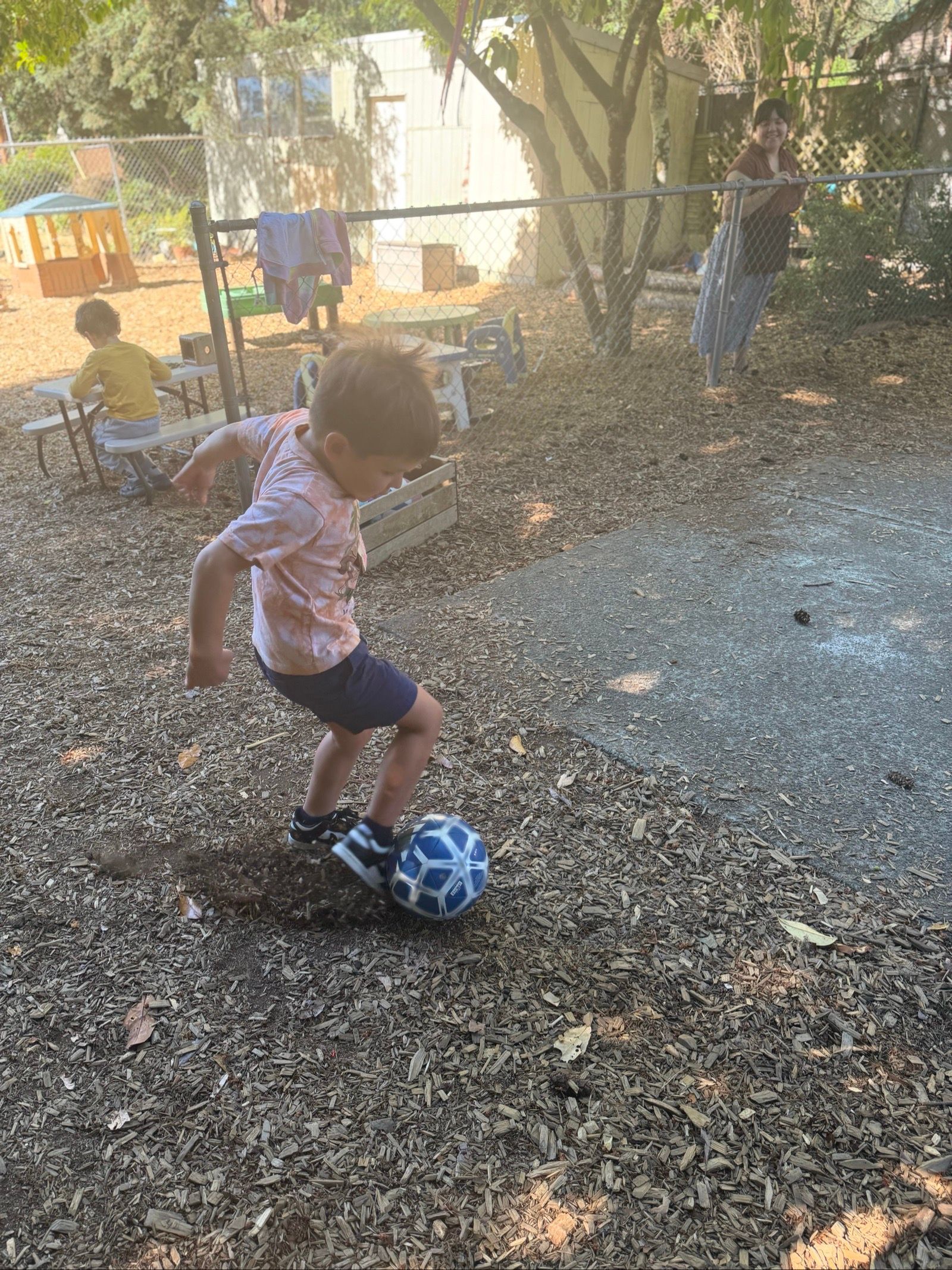 Child dribbling a blue-and-white soccer ball on a leaf-covered yard outdoors