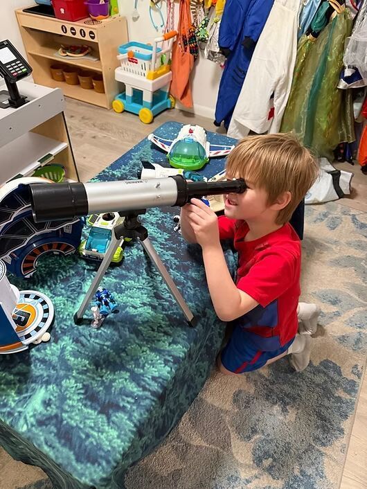 Child looking through a telescope on a tripod in a playroom