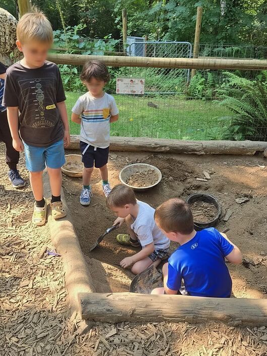 Children playing in a dirt sandbox outdoors, digging and exploring near wooden borders.