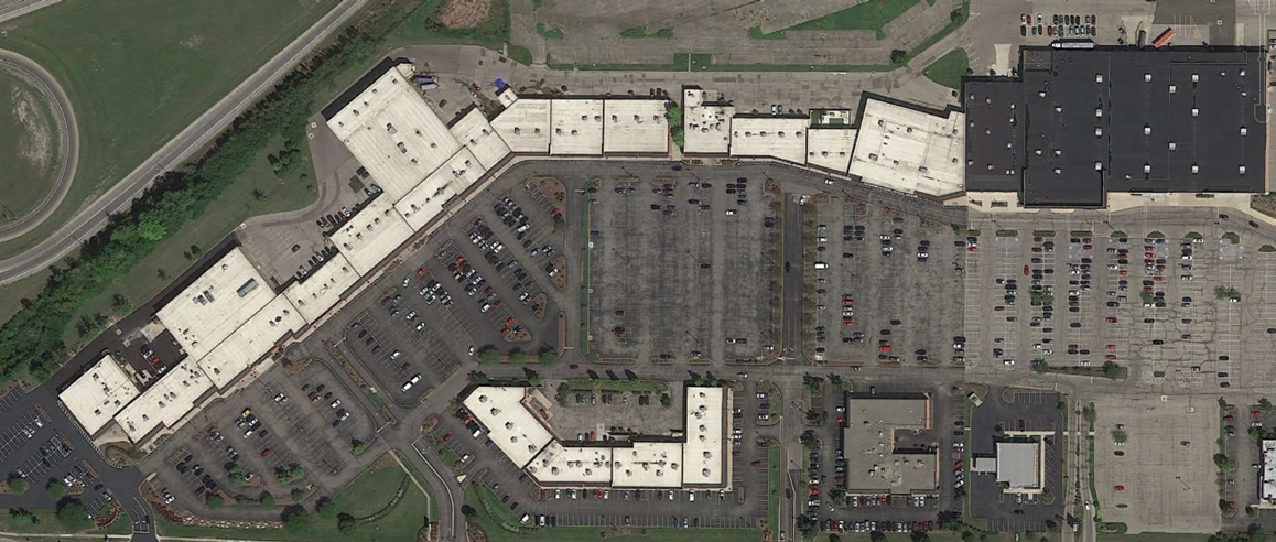 Aerial view of a large shopping mall with parking lots and surrounding roads.