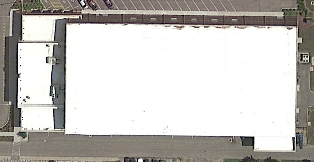 Aerial view of a large white-roofed rectangular warehouse building with adjacent parking areas.