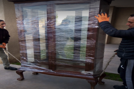 Dos personas envuelven un gran armario de madera en plástico transparente para su mudanza.