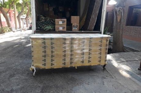 Palés de productos envueltos en plástico retráctil apilados en un almacén junto a una carretilla elevadora.