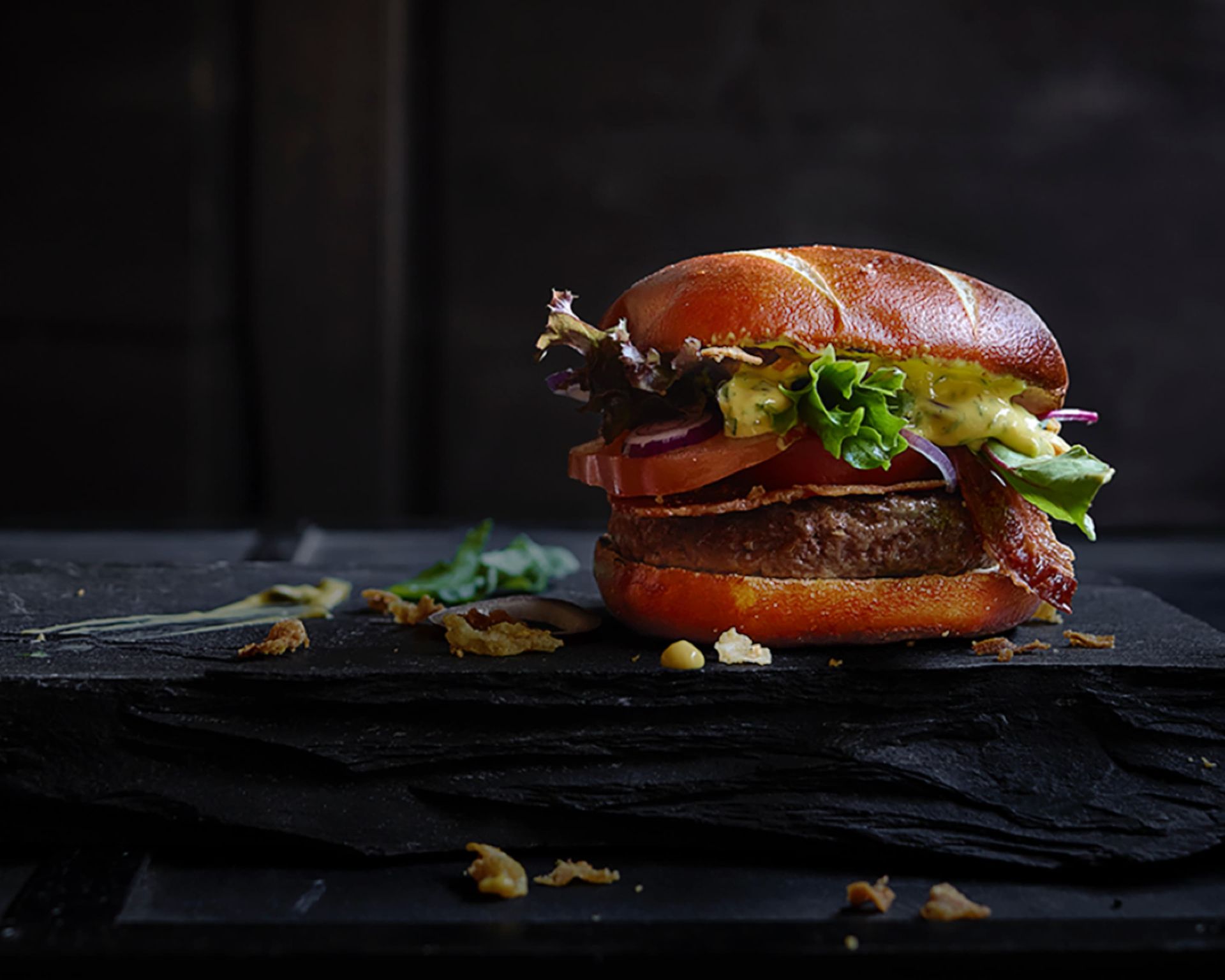 Gros plan d'un hamburger garni de laitue et de sauce, posé sur une surface en ardoise sombre. - Burger Choice livraison Uccle