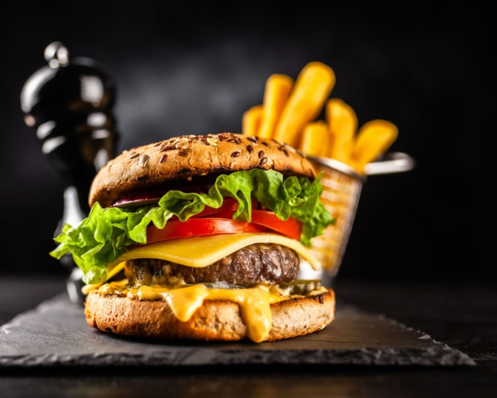 Cheeseburger grillé avec laitue, tomate et frites sur une ardoise, sur fond sombre. - Burger Choice livraison Uccle
