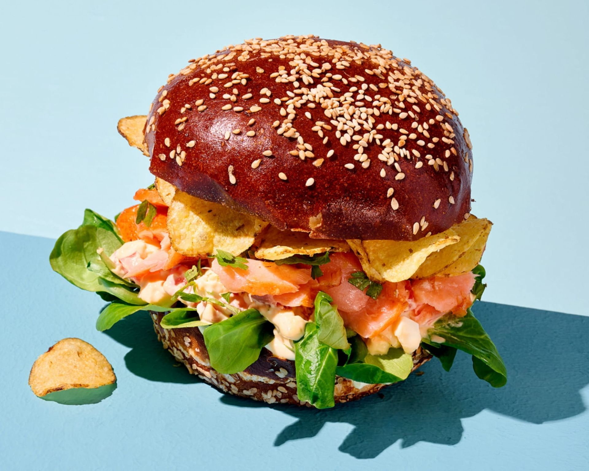 Burger aux graines de sésame avec laitue, tomate et sauce sur fond bleu clair
