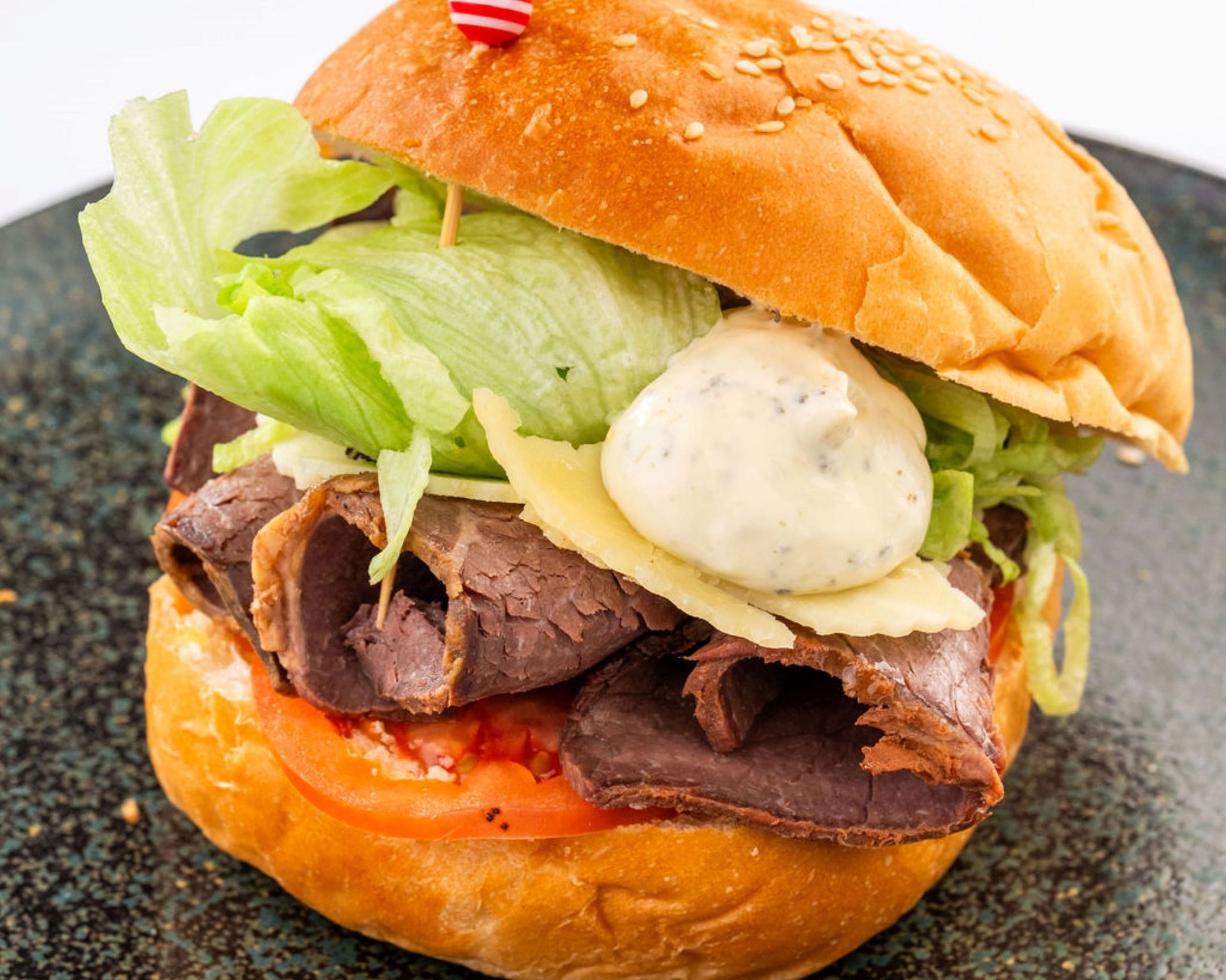 Gros plan sur un hamburger avec laitue, tomate, rôti de bœuf, fromage et sauce sur un pain.  Slice Beef Burger Choice Uccle