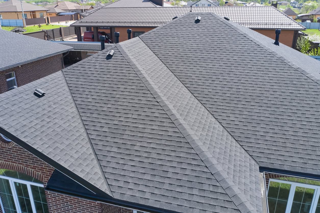 Gray shingled house roof with multiple ridges and skylight vents, seen from above