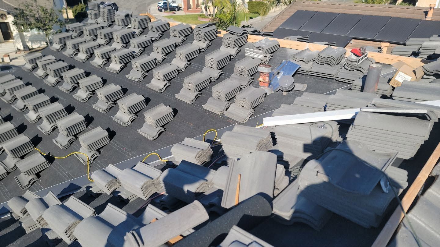 Rows of gray roof tiles stacked outdoors at a factory or yard, with a few workers and equipment nearby
