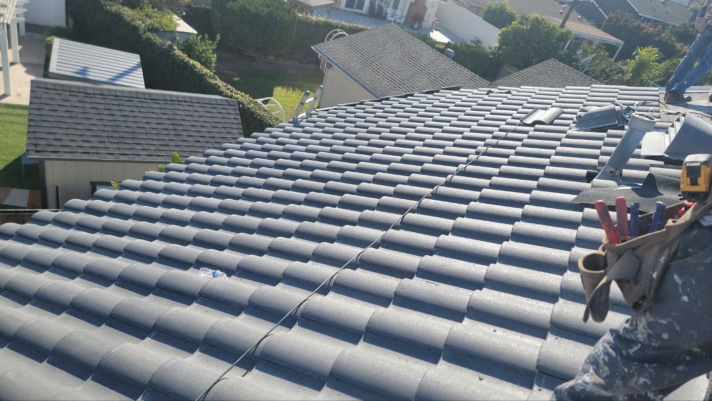Workers installing gray roof tiles on a sloped rooftop in a residential neighborhood