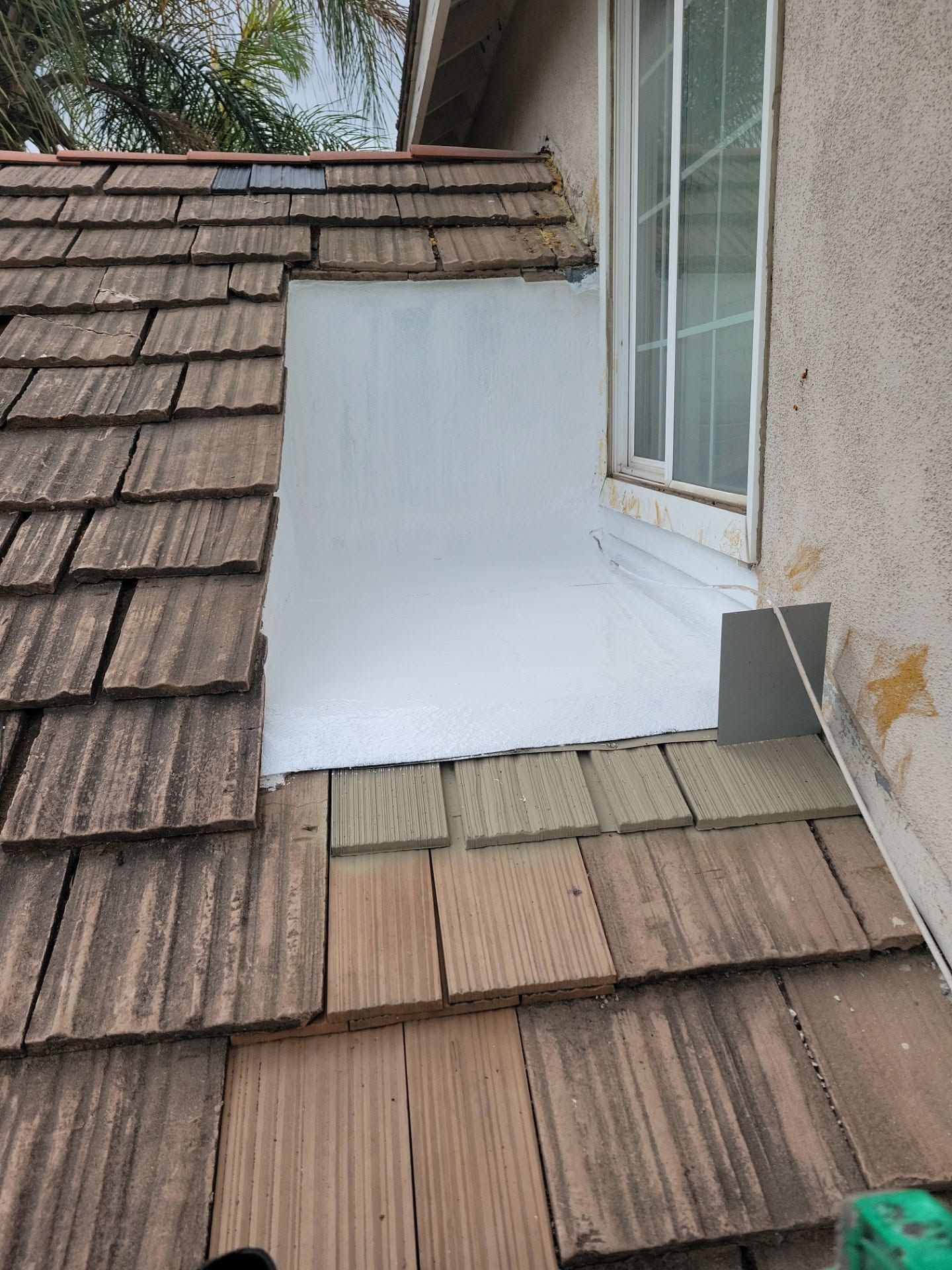 Roofing repair around a white dormer window on a shingled roof