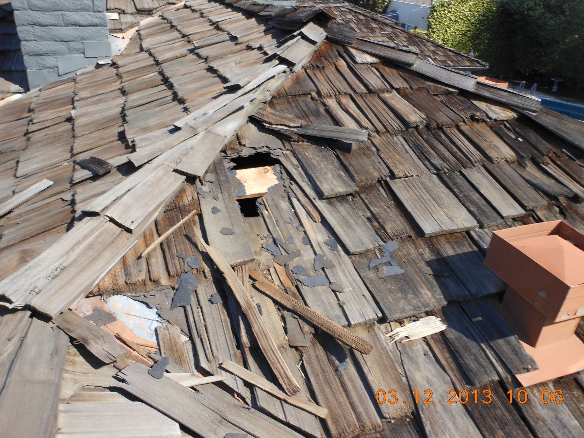 Rooftop with broken, weathered wooden shingles and visible damage near a chimney.