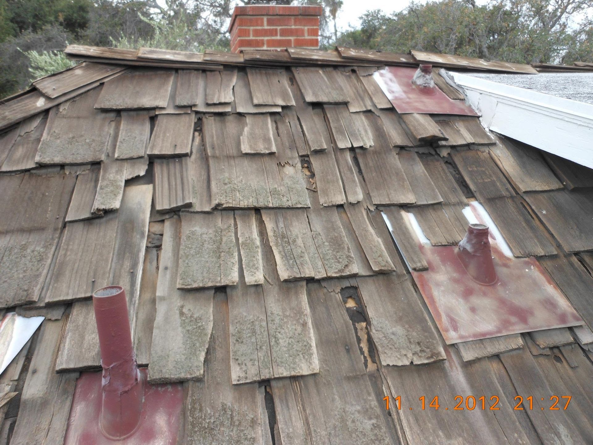 Weathered shingle roof with damaged patches, red chimney, and two metal vents near the ridge.