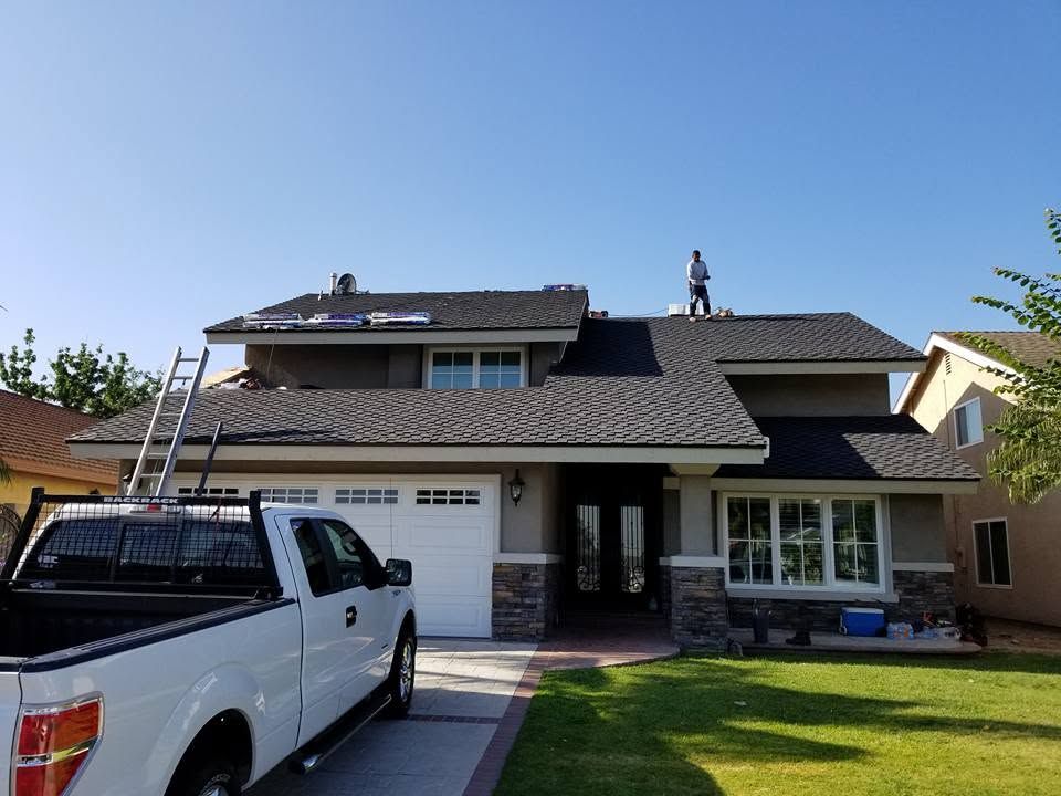 White pickup truck parked in front of a house with a roof under repair and a ladder on the side