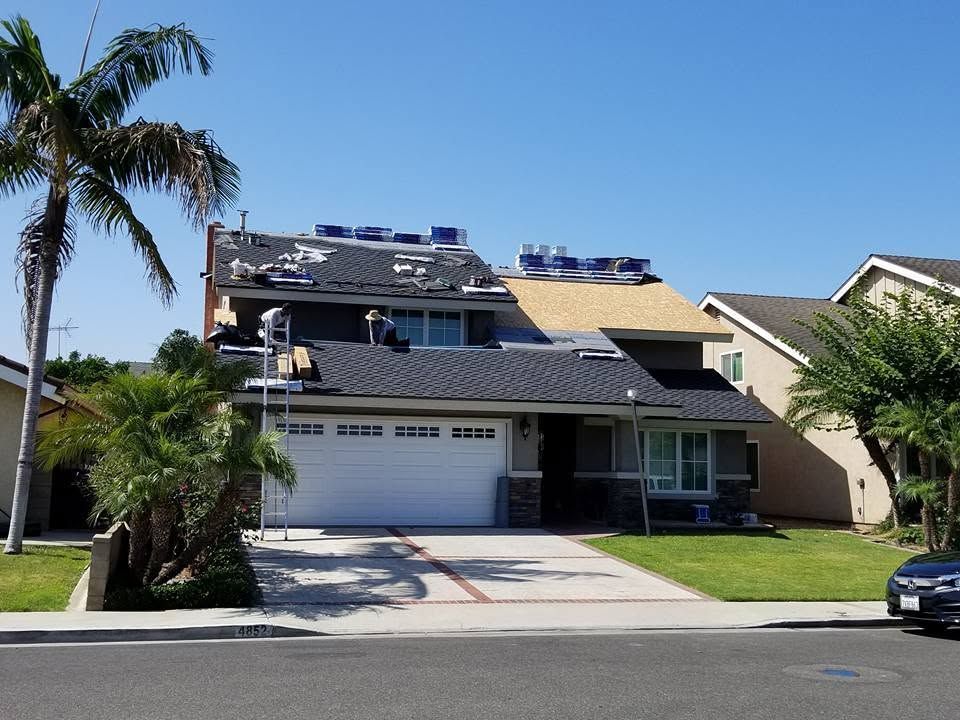 Suburban two-story house with solar panels, white garage, palm trees, and a blue car parked outside