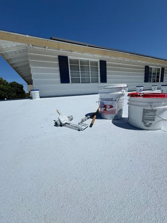 Roof coated with white foam, with paint buckets and tools on a sunny rooftop.