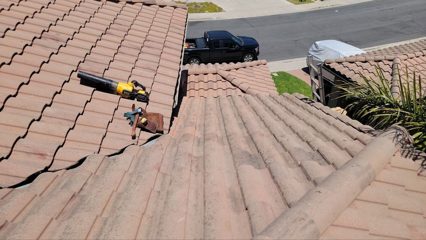 Roof worker using a yellow tool on a tiled roof, with a black car in the background.