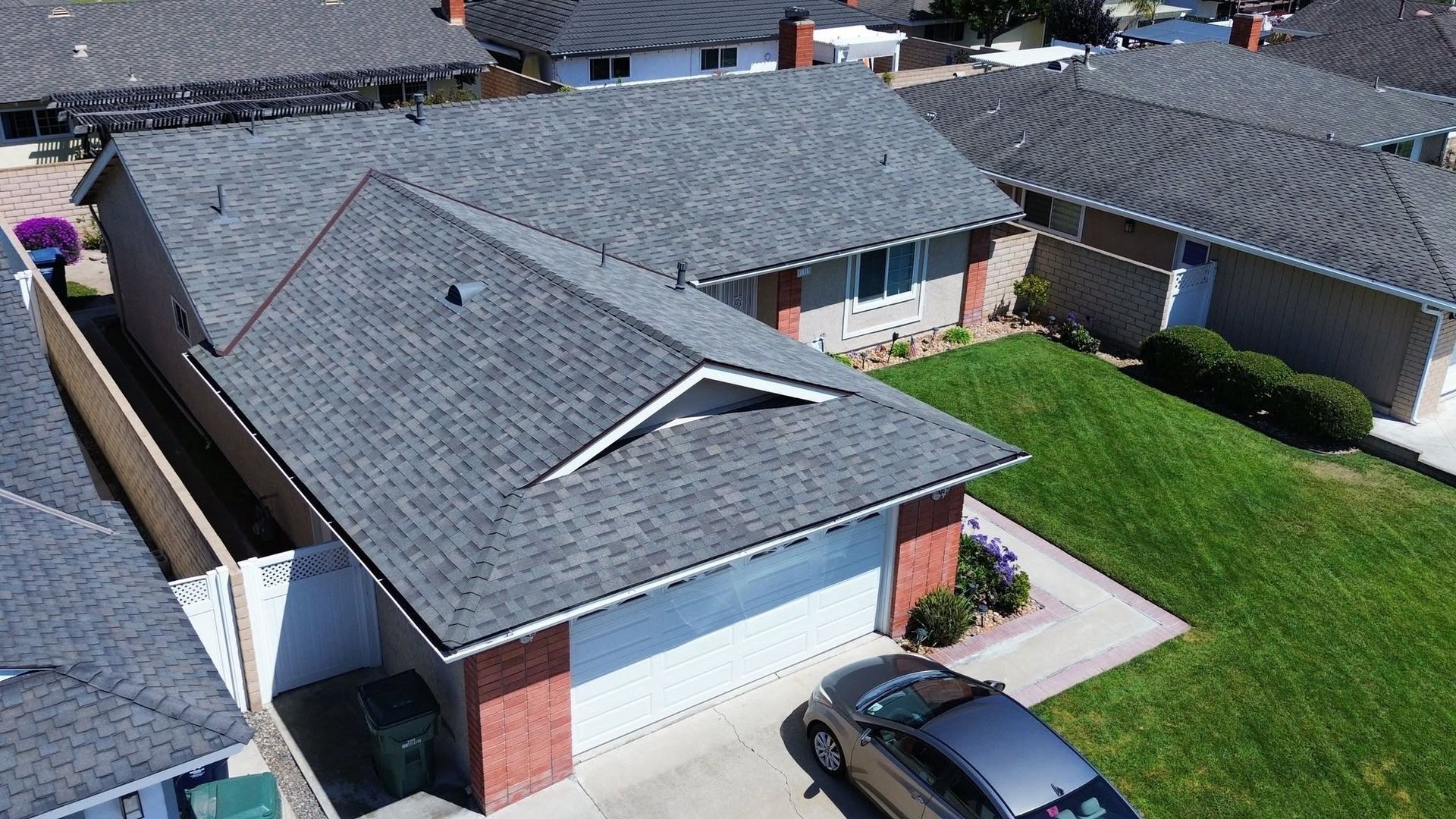 Aerial view of a suburban house with gray roof, white garage, brick accents, and a parked car in the driveway