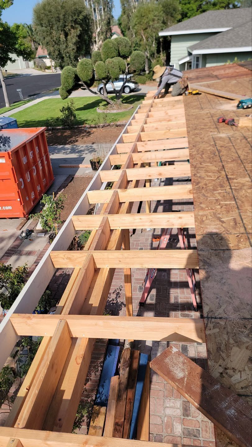 Wooden deck framing under construction beside a house, with lumber beams and concrete supports.