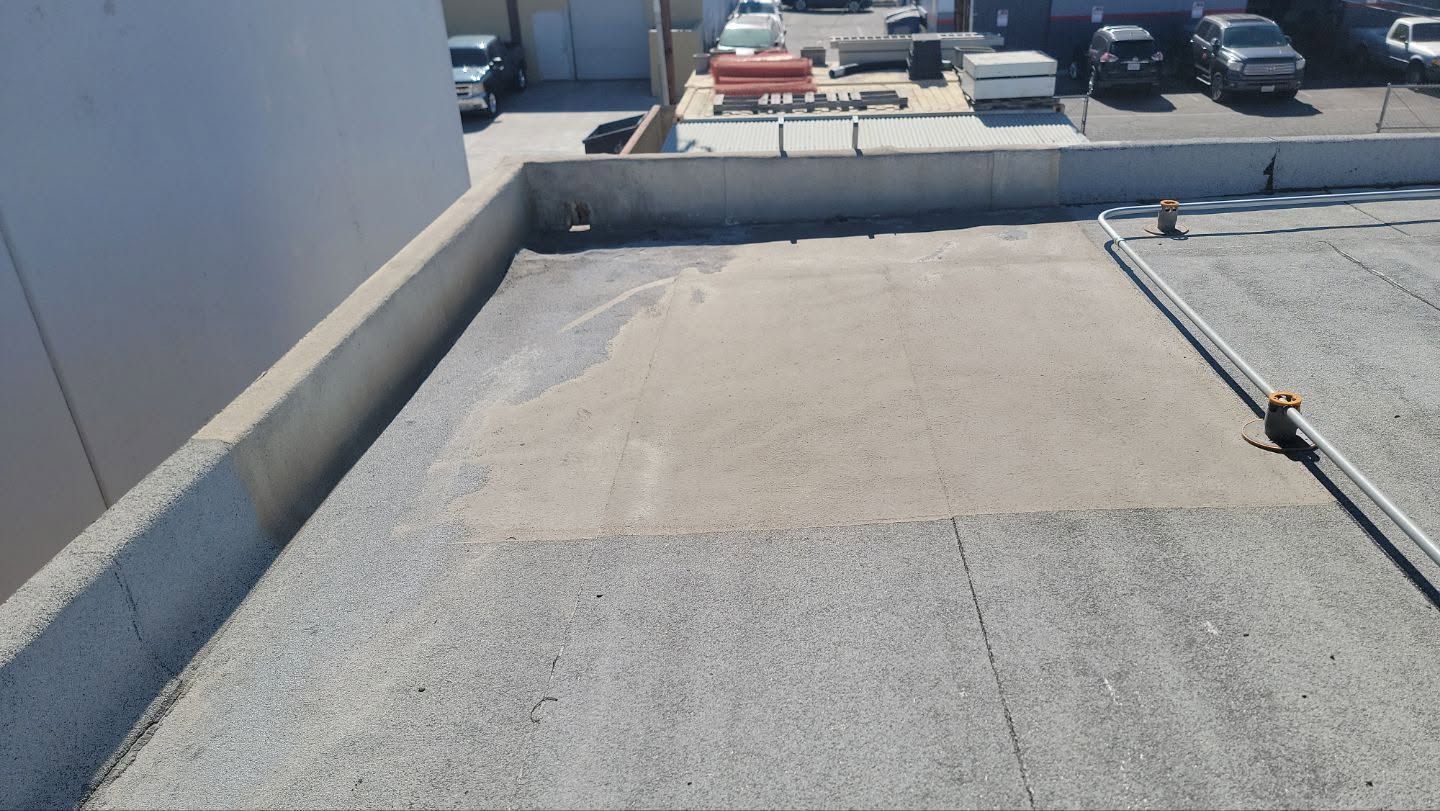 Flat gravel rooftop with low concrete walls, HVAC units, and parked cars in the distance.
