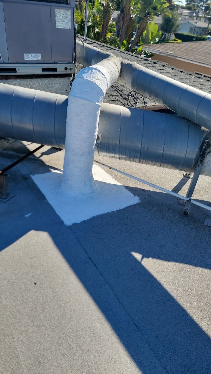 White roof vent pipe on a flat rooftop beside railings and tracks, with bright sunlight and long shadows.