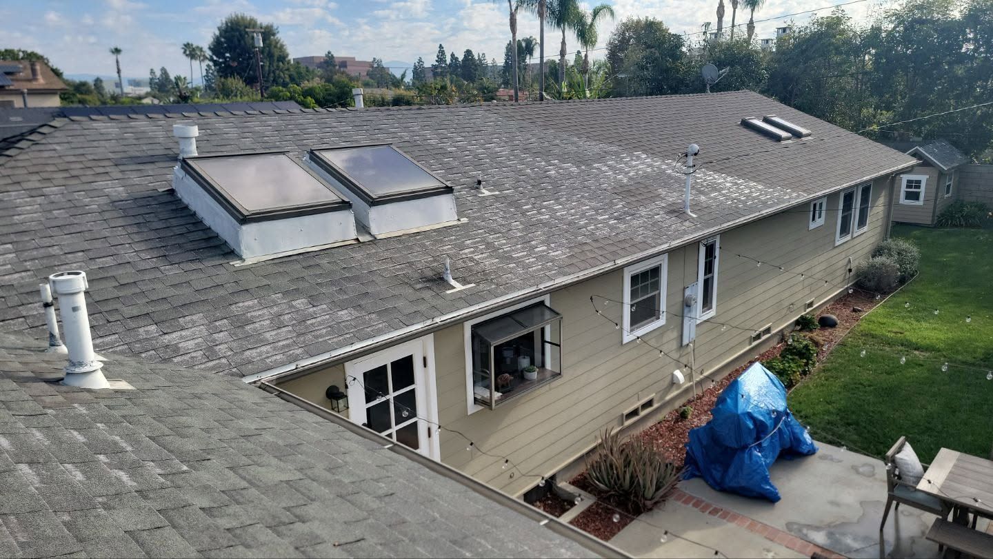 Rooftop with gray shingles and skylights, showing a row of house windows and a blue tarp below